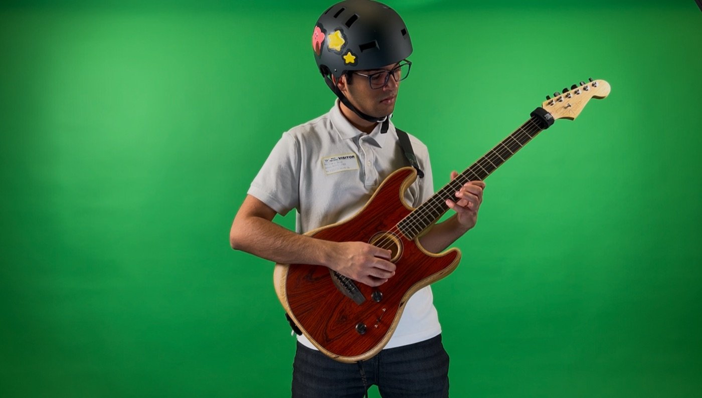 R.C. Napkin playing a red electric guitar in front of a green screen, wearing a star-covered helmet